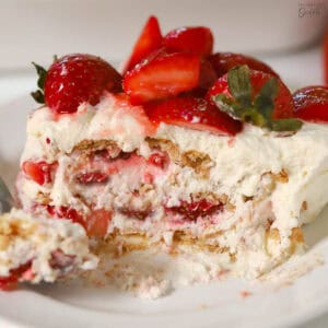 Slice of a strawberry icebox cake topped with fresh strawberries on a white plate.