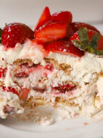 Slice of a strawberry icebox cake topped with fresh strawberries on a white plate.