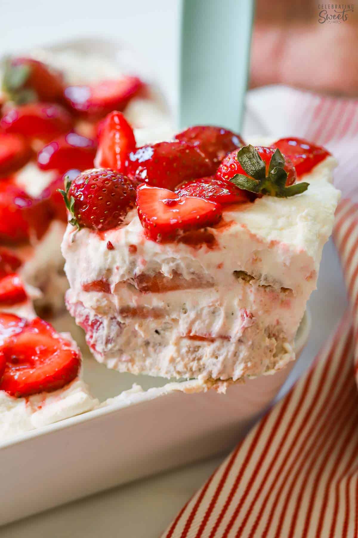 Slice of strawberry icebox cake on a spatula being scooped out of a white baking dish.