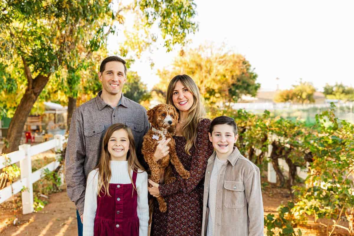 A man, woman, boy, and girl, with a brown dog standing outside under a tree.