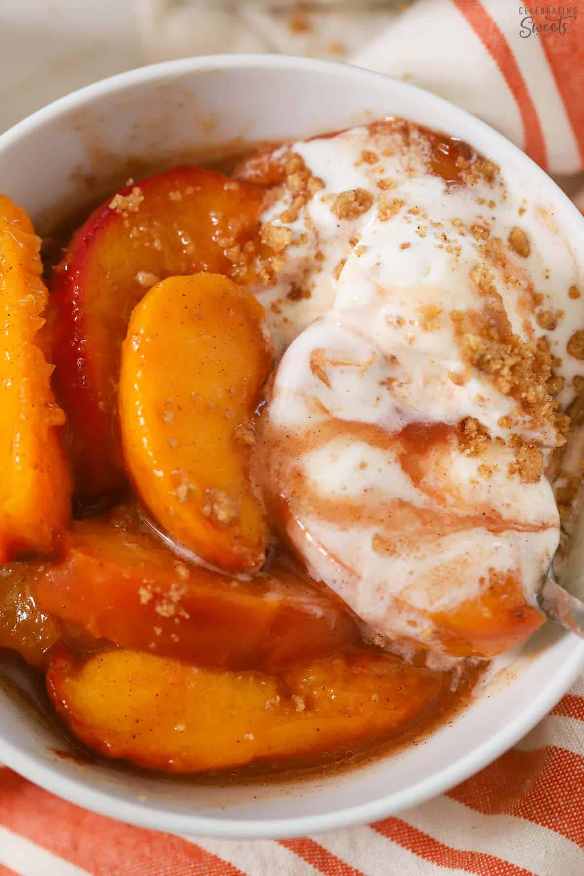 Baked peaches in a white bowl topped with slightly melted vanilla ice cream.