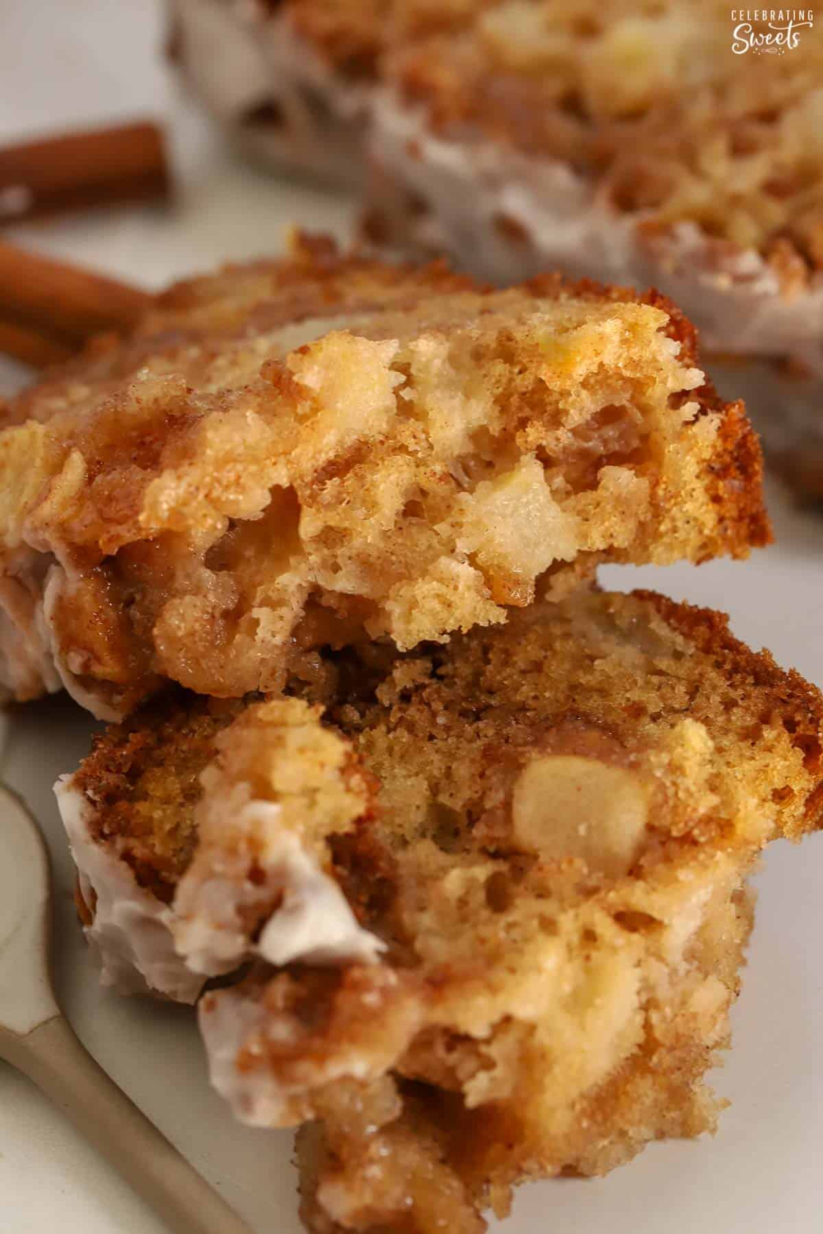 Two pieces of apple fritter bread stack on each other next to a spoon of icing.