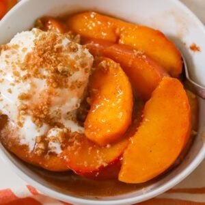 Baked peaches in a white bowl with vanilla ice cream.