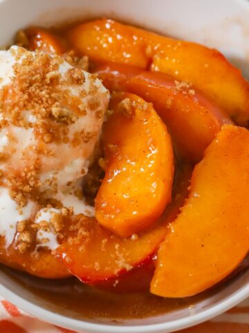 Baked peaches in a white bowl with vanilla ice cream.