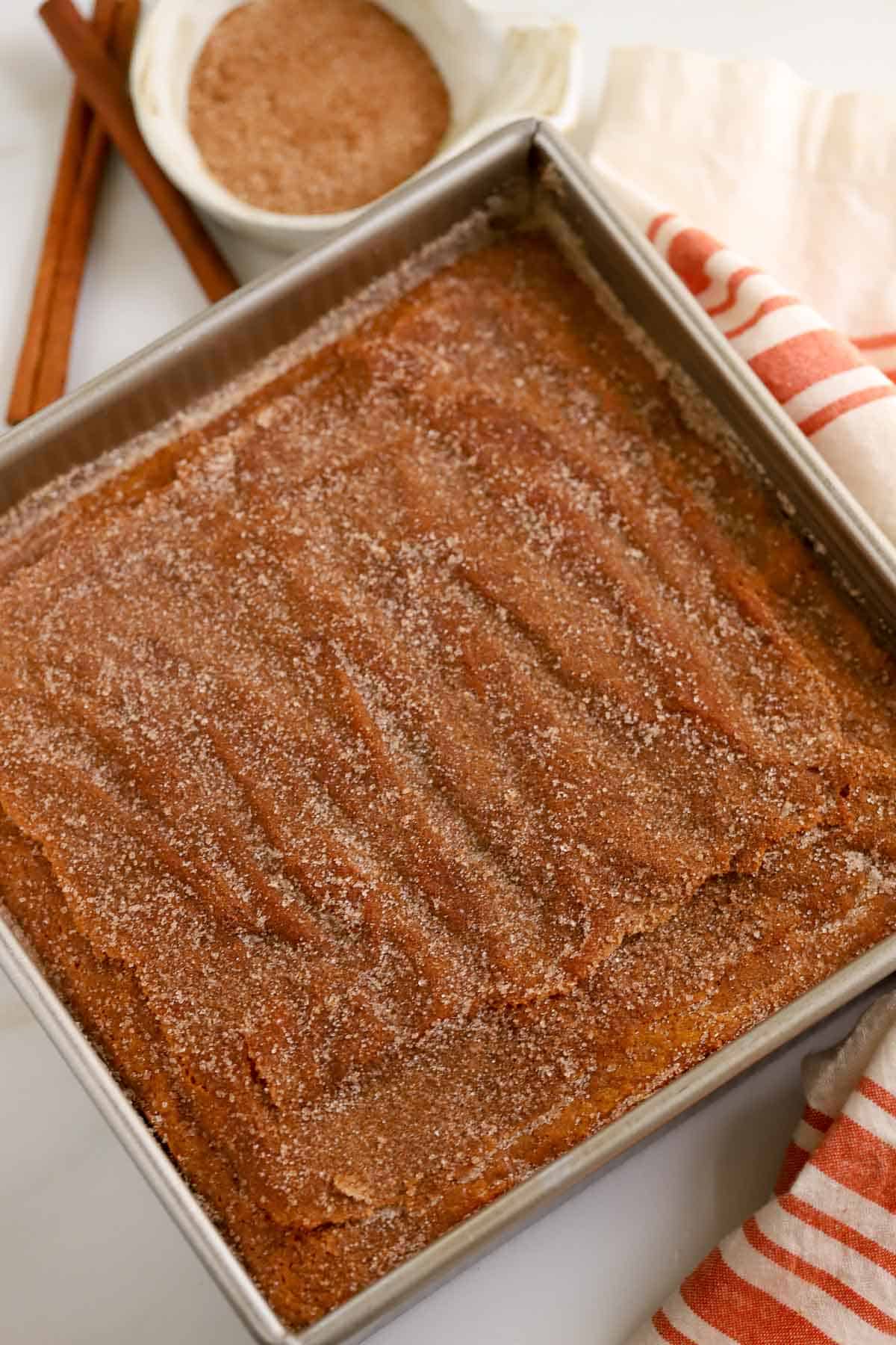 Pumpkin cake topped with cinnamon sugar in a square aluminum pan.