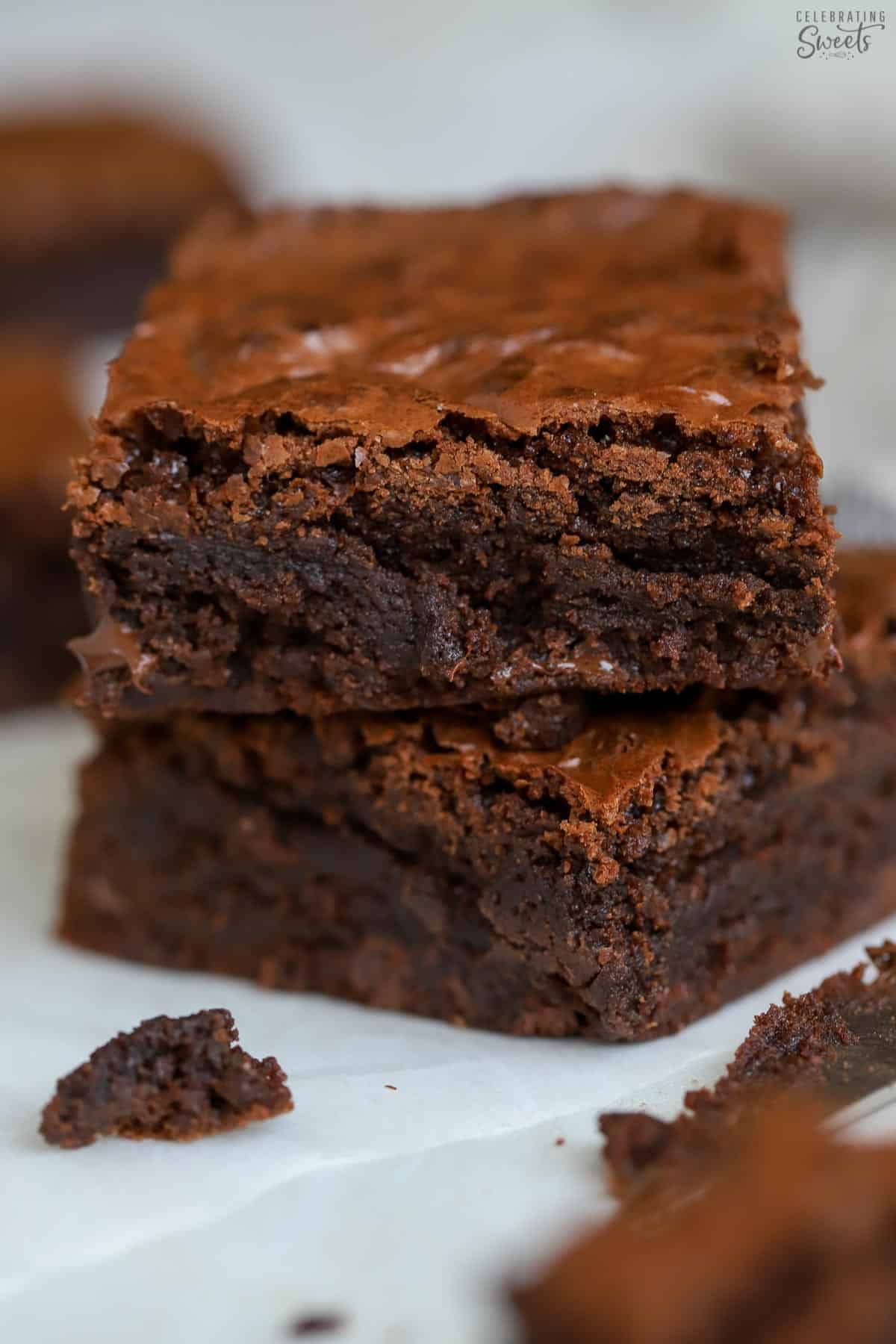 Two brownies stacked on top of each other on a piece of white parchment paper.