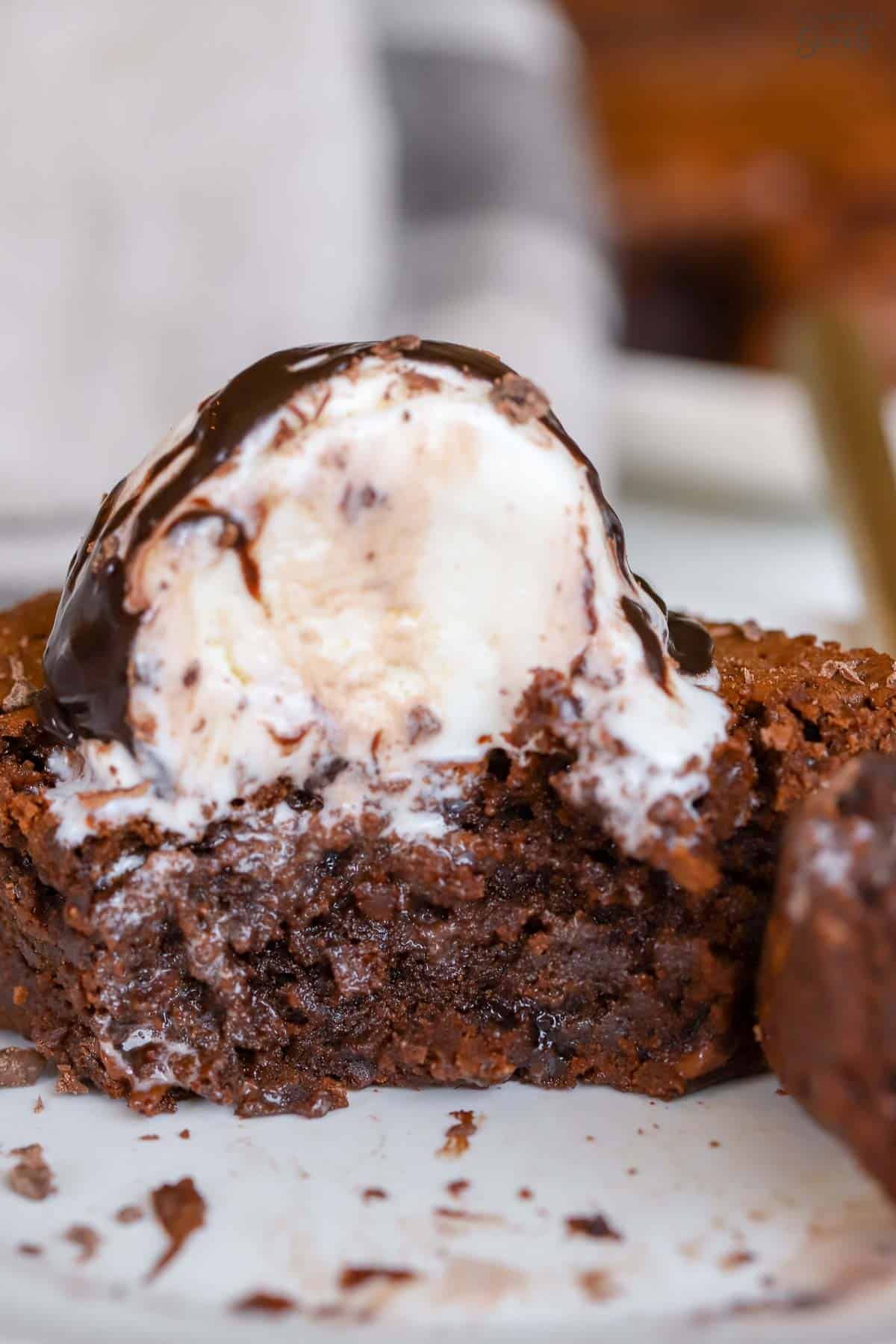 Partially eaten brownie on a white plate topped with vanilla ice cream.