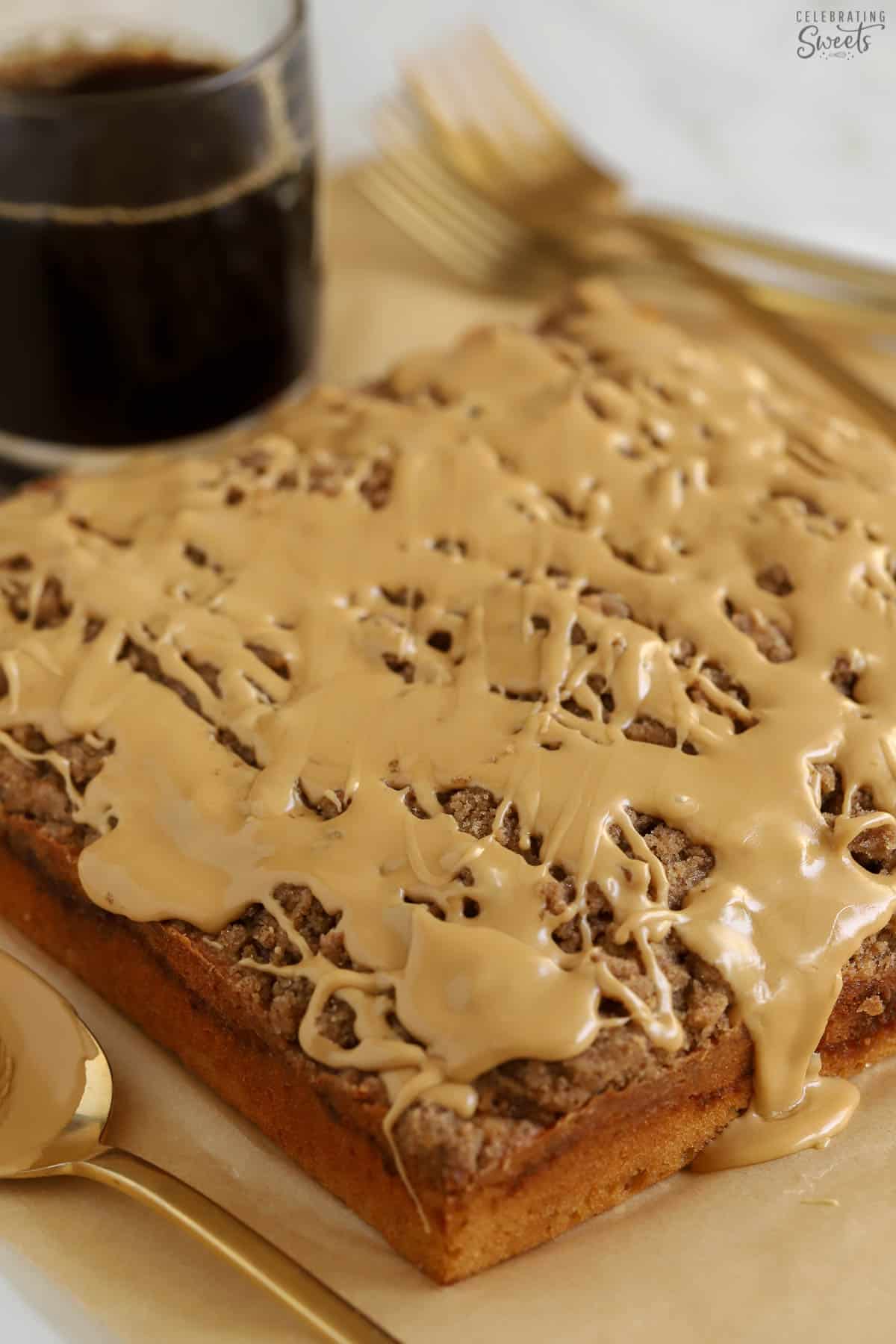 A large crumb cake on a piece of brown parchment paper next to gold silverware and a cup of coffee.