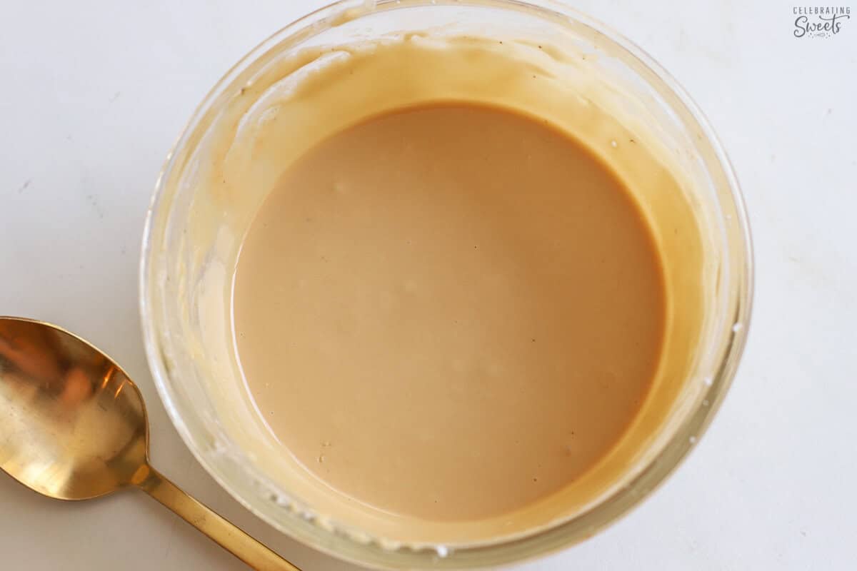 Glass bowl filled with beige icing next to a gold spoon.