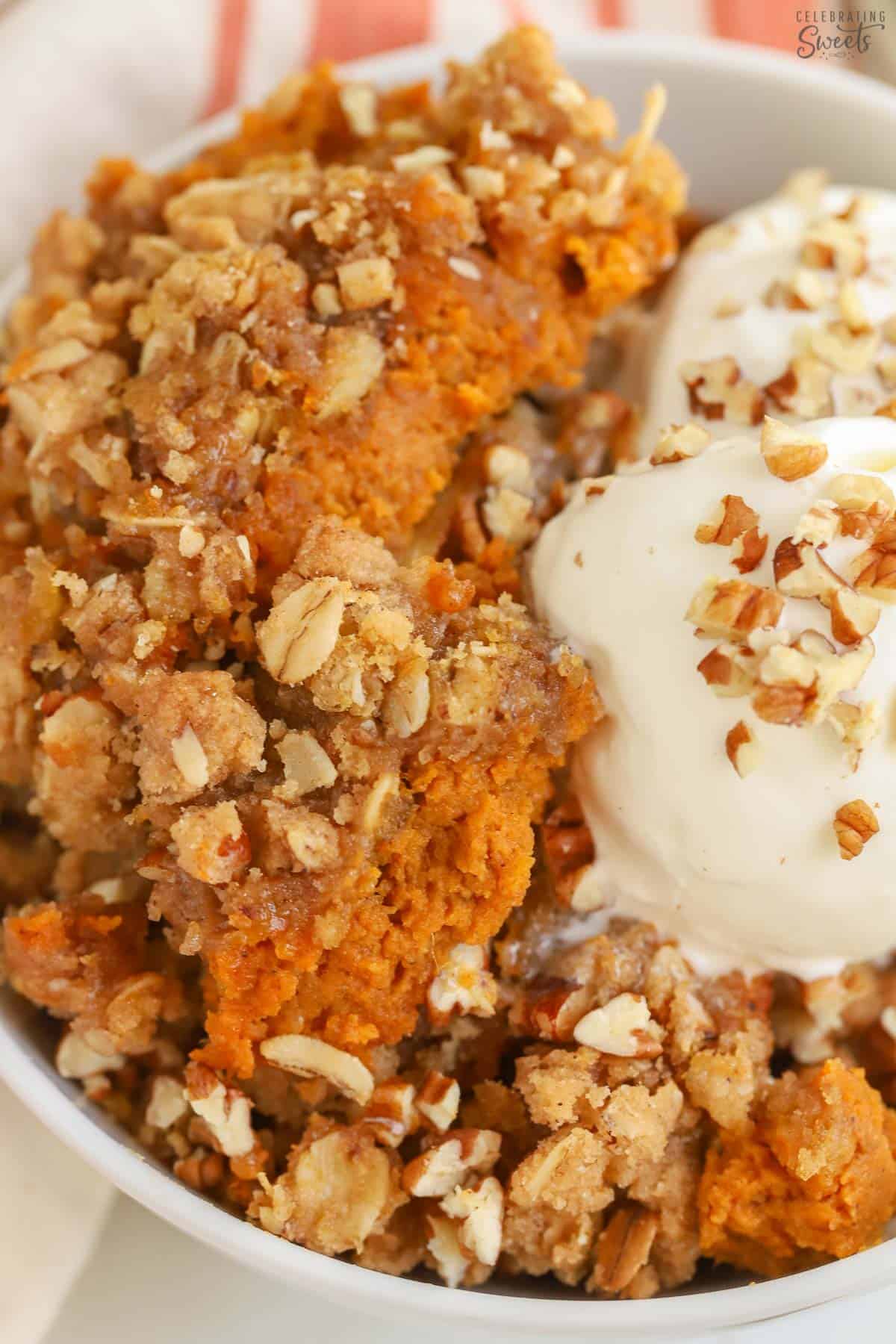 Closeup of a pumpkin crisp in a white bowl topped with a scoop of vanilla ice cream and pecans.