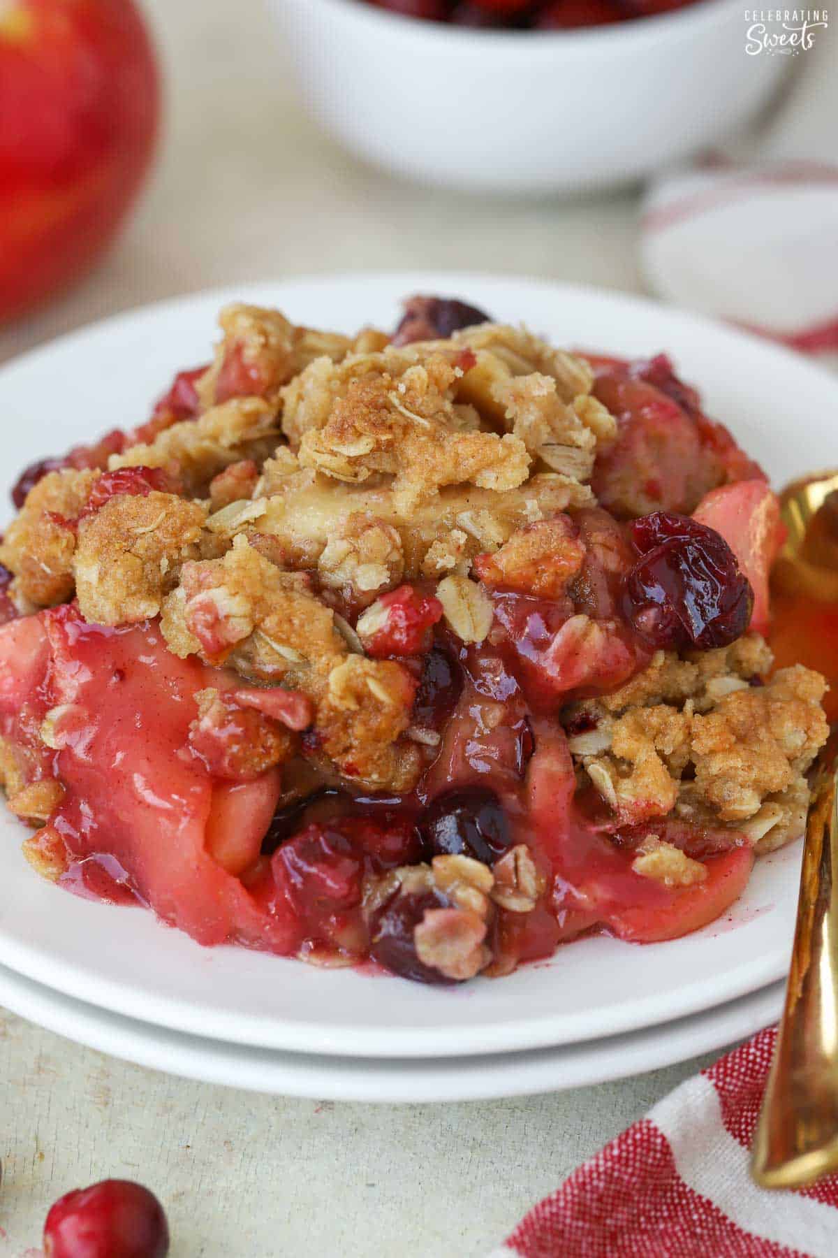 Apple cranberry crisp on a white plate with a gold spoon.