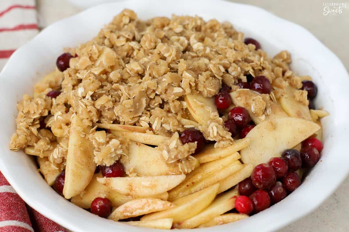 Unbaked apple cranberry crisp in a white baking dish next to a red striped napkin.