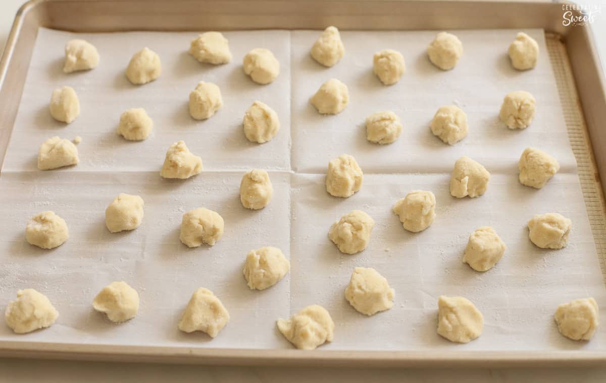 Mini sugar cookie dough balls on a parchment lined baking sheet.