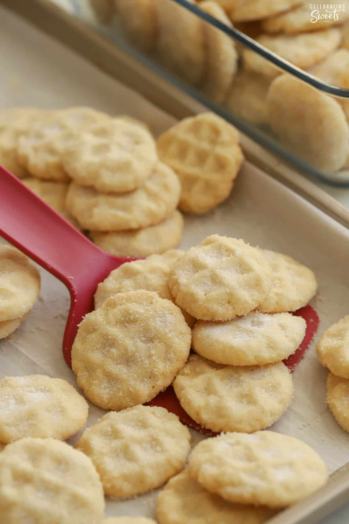 Mini sugar cookies on a red spatula set on a baking sheet.