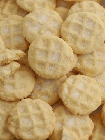 A pile of mini sugar cookies on a baking sheet.