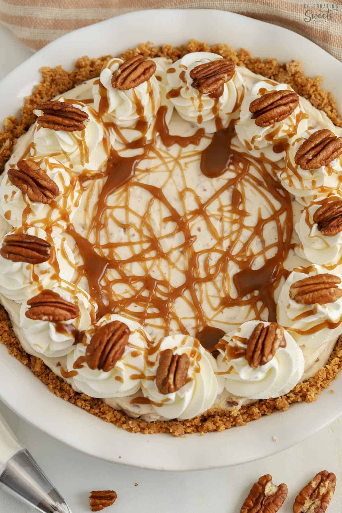 Overhead photo of a pecan pie cheesecake in a white pie plate decorated with caramel sauce and pecans.