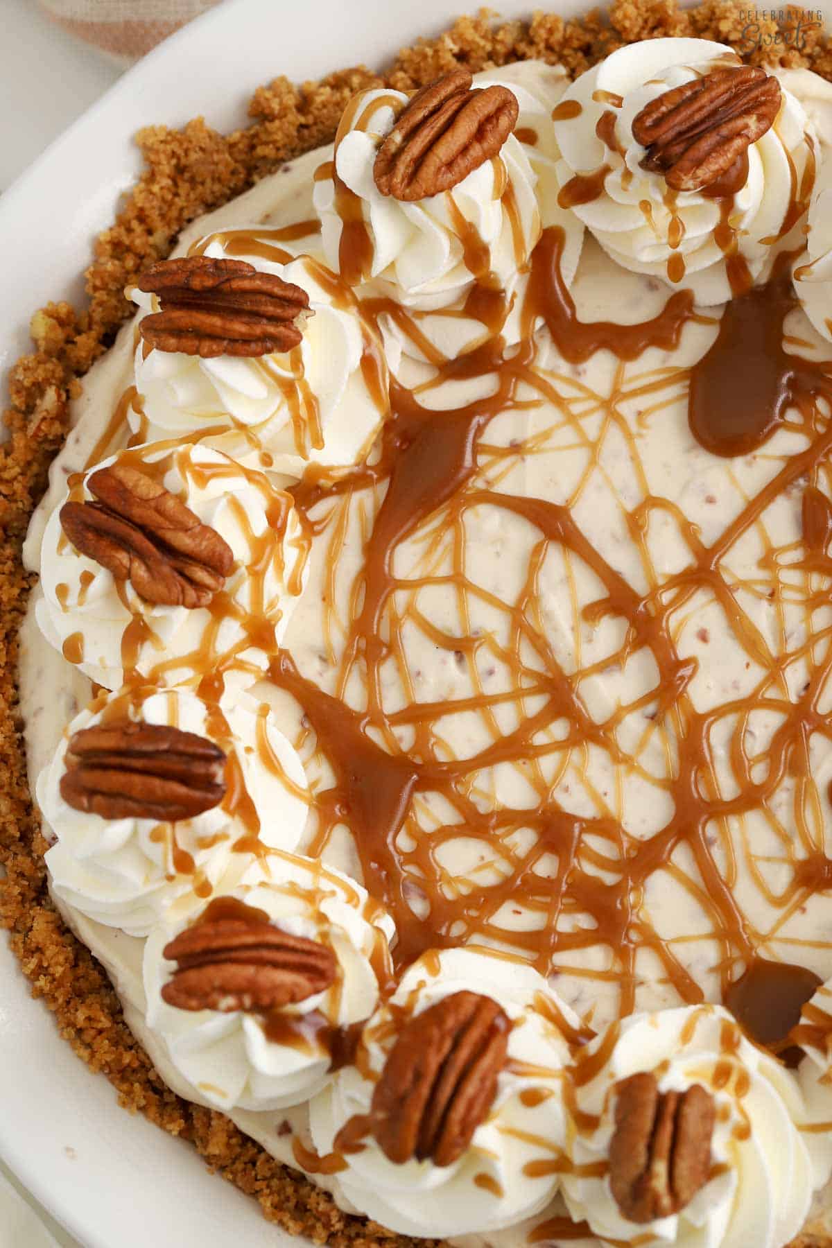 Overhead photo of a pecan pie cheesecake in a white pie plate decorated with caramel sauce and pecans.