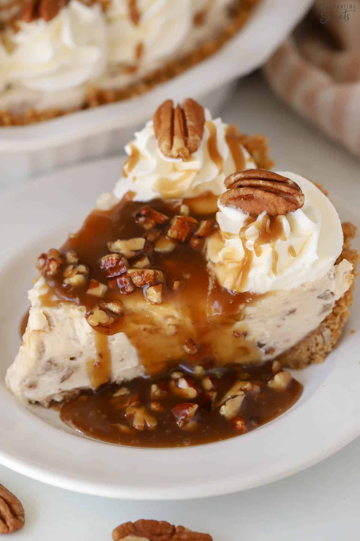 A slice of pecan pie cheesecake topped with caramel sauce on a white plate.