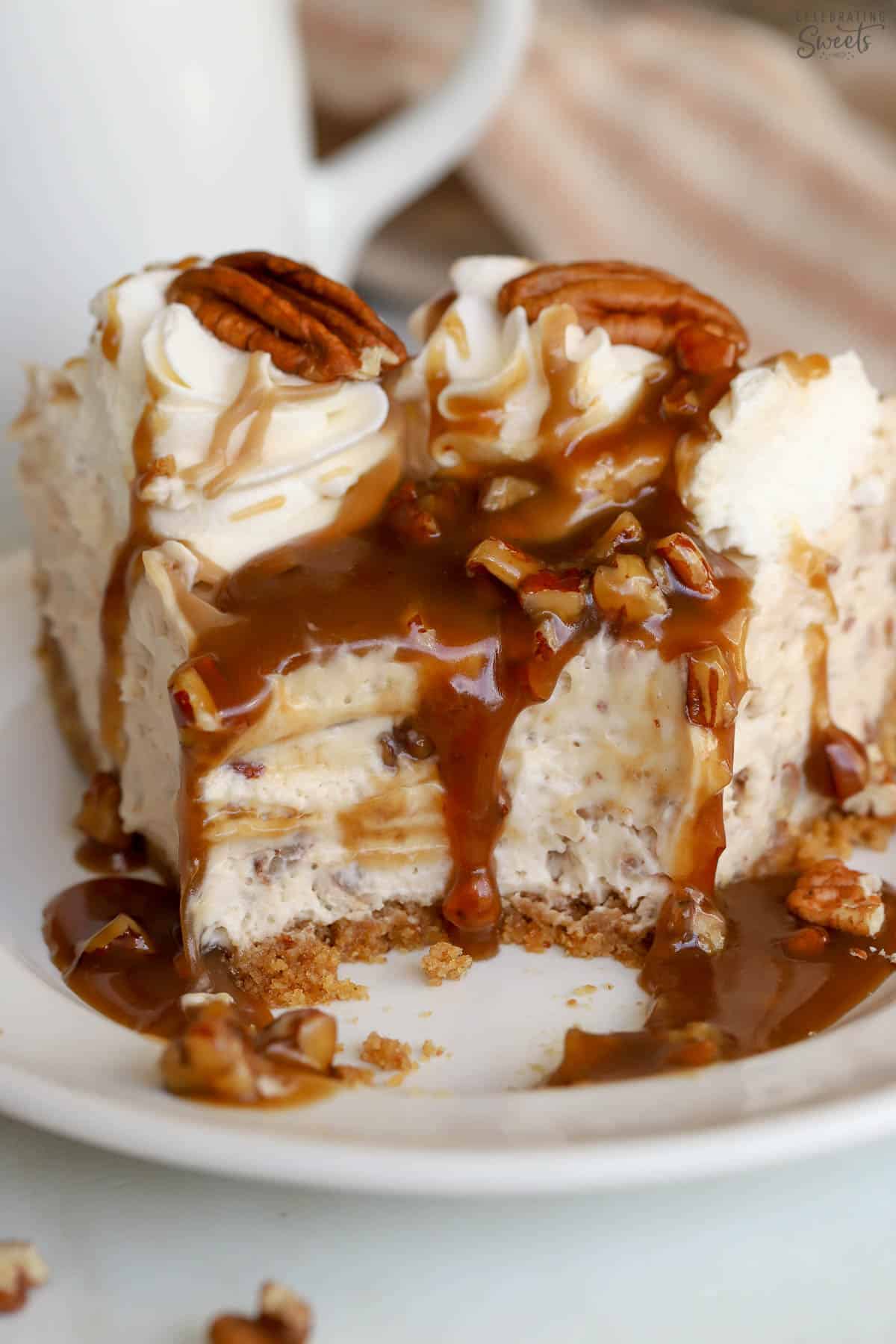 A slice of pecan pie cheesecake topped with caramel sauce on a white plate.