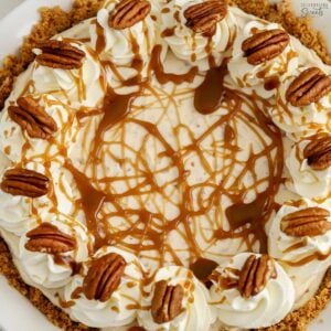 Overhead photo of a pecan pie cheesecake in a white pie plate decorated with caramel sauce and pecans.