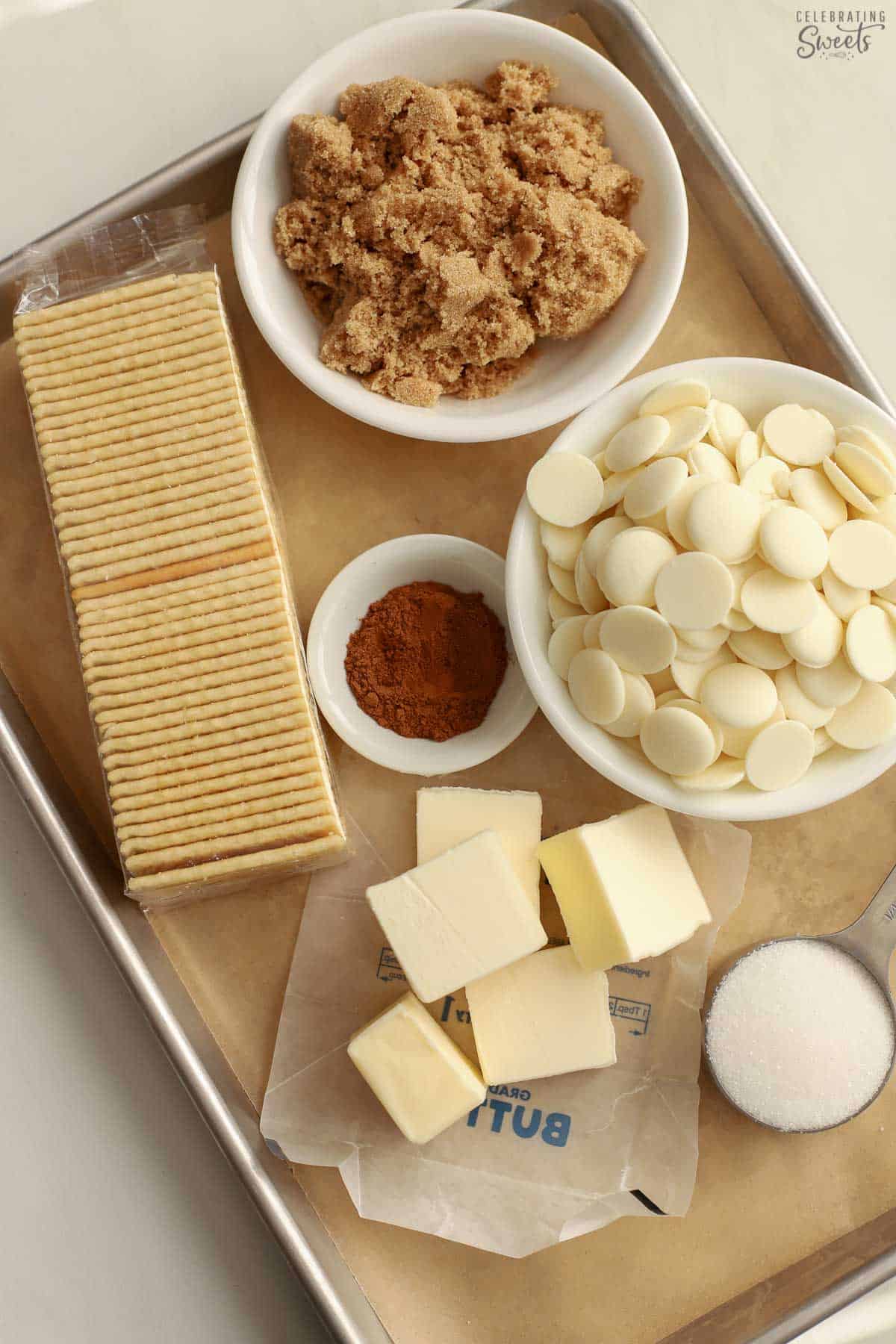 Ingredients for churro toffee on a baking sheet: butter, sugars, crackers, cinnamon, white chocolate wafers.