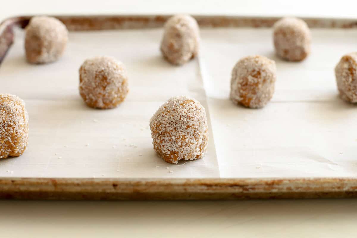 Sugar covered ginger molasses cookie dough balls on a parchment-lined baking sheet.