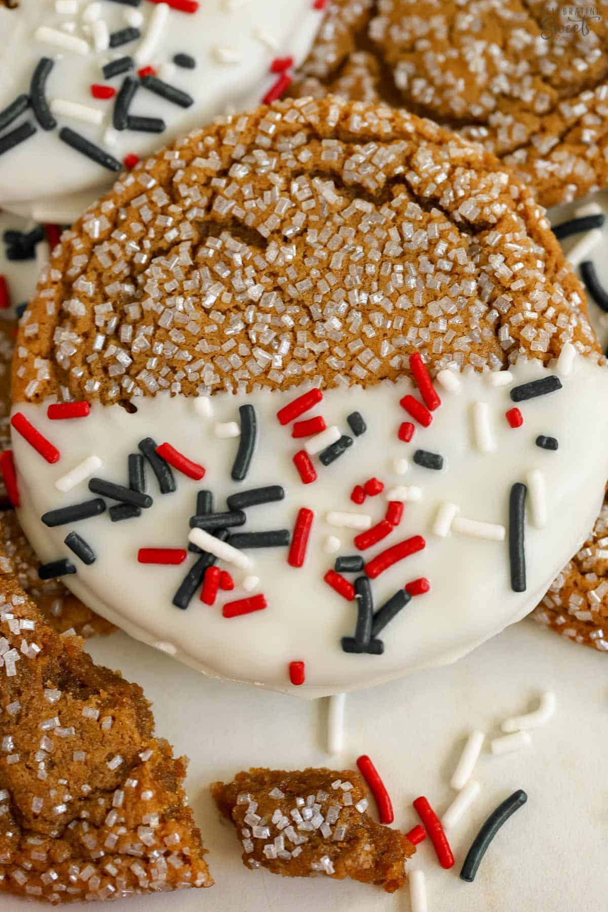 Closeup of a ginger molasses cookie dipped in white chocolate and covered in red and green sprinkles.