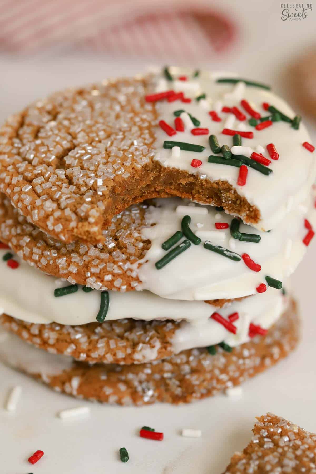 Stack of ginger molasses cookies dipped in white chocolate and covered in red and green sprinkles.