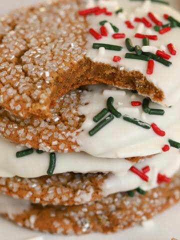 Stack of ginger molasses cookies dipped in white chocolate and covered in red and green sprinkles.