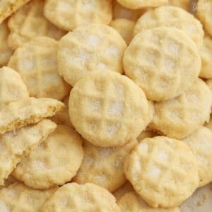 Mini sugar cookies covered in sugar piled on a baking sheet,