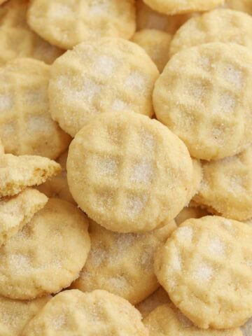 Mini sugar cookies covered in sugar piled on a baking sheet,
