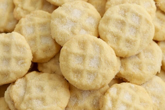 Mini sugar cookies covered in sugar piled on a baking sheet,