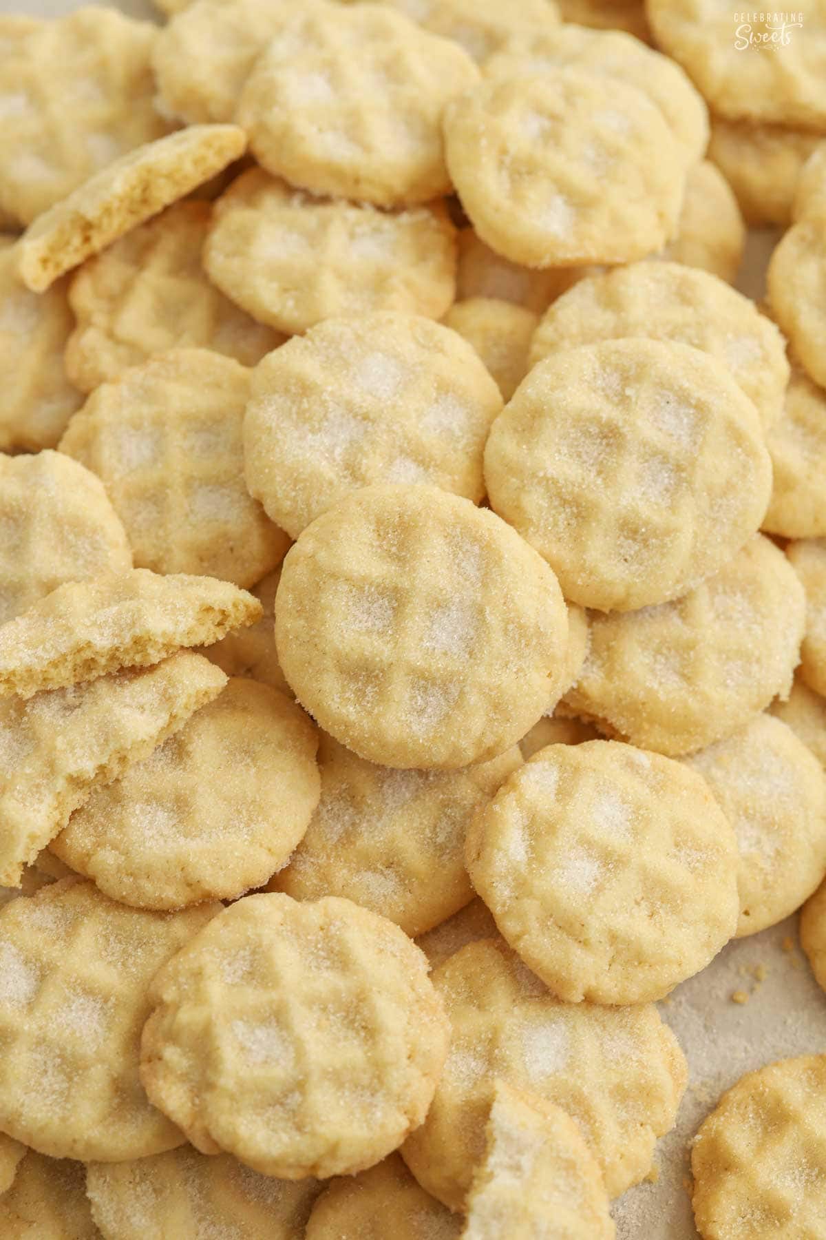 Mini sugar cookies covered in sugar piled on a baking sheet,