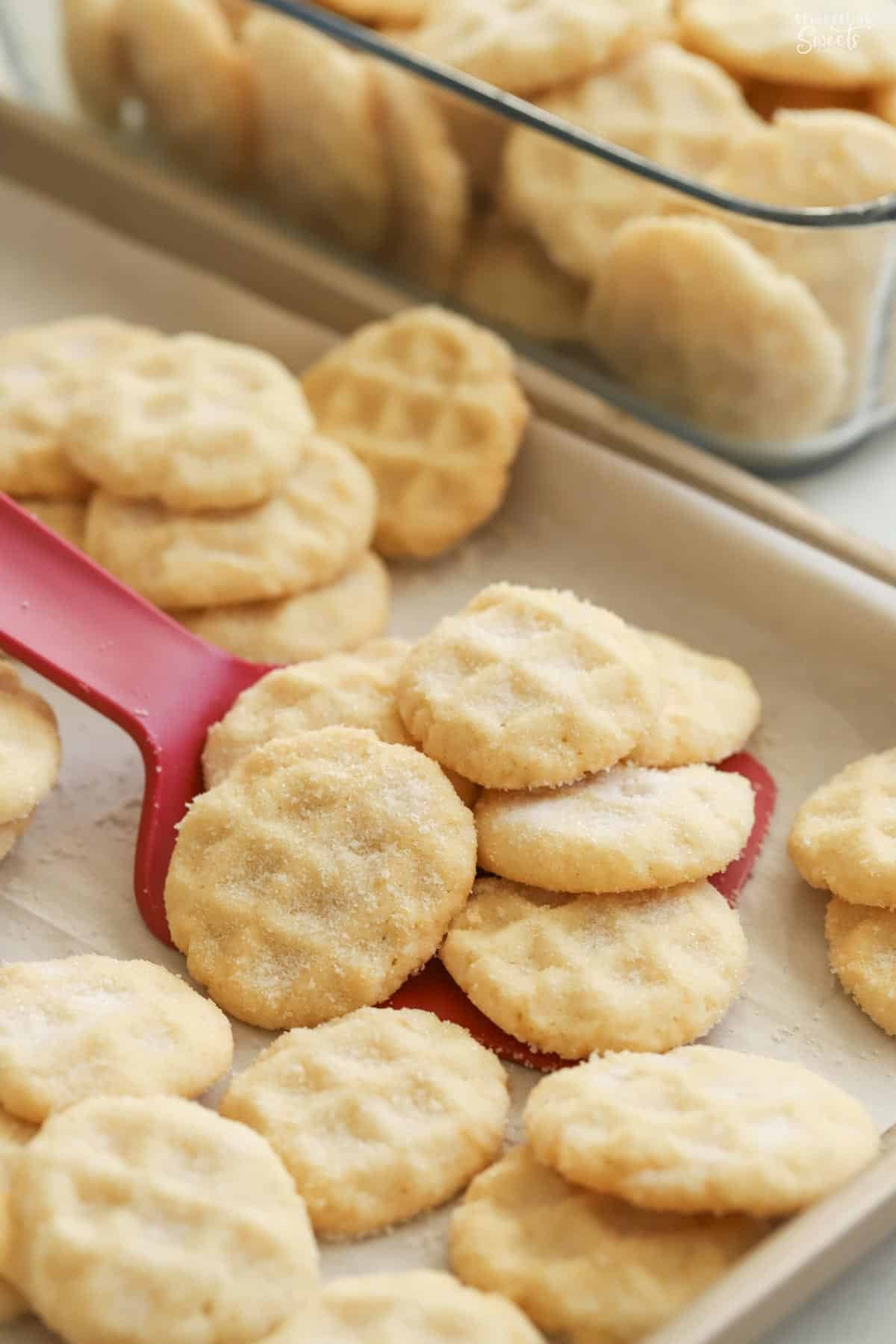 A pile of mini sugar cookies on a red spatula on a baking sheet.