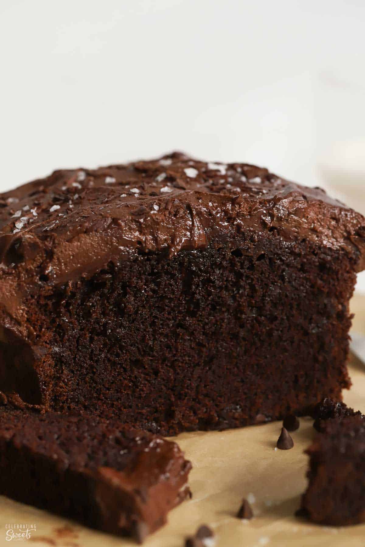 Chocolate loaf cake topped with chocolate frosting on a piece of parchment paper.