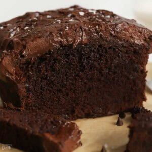 Chocolate loaf cake topped with chocolate frosting on a piece of parchment paper.