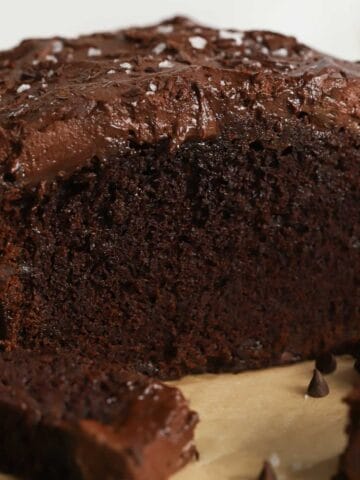 Chocolate loaf cake topped with chocolate frosting on a piece of parchment paper.