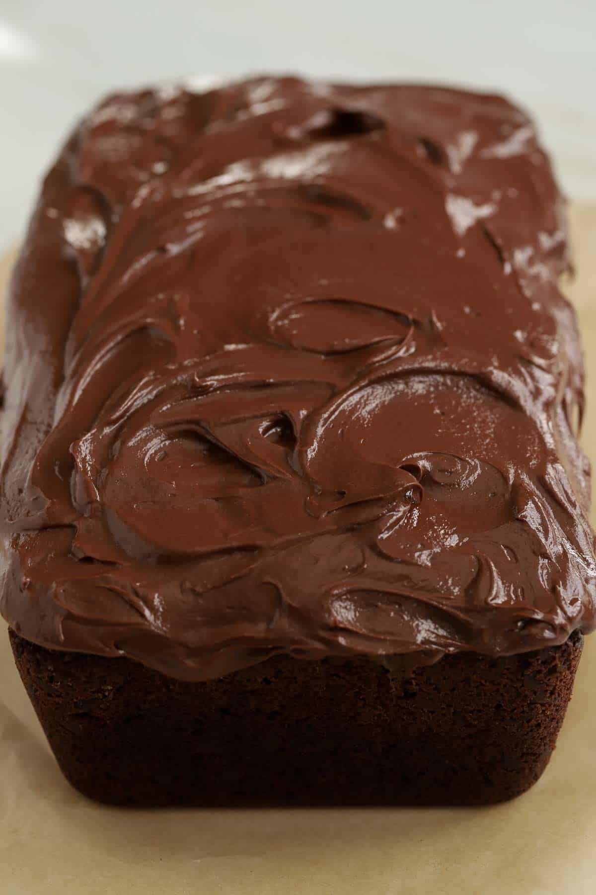 Chocolate loaf cake topped with glossy chocolate frosting sitting on a piece of parchment paper.