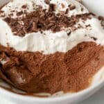 Close up of chocolate mousse topped with whipped cream and chocolate shavings in a white bowl.