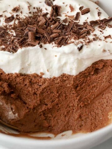 Close up of chocolate mousse topped with whipped cream and chocolate shavings in a white bowl.