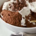 Gold spoon with chocolate mousse and whipped cream sitting on the edge of a white bowl.