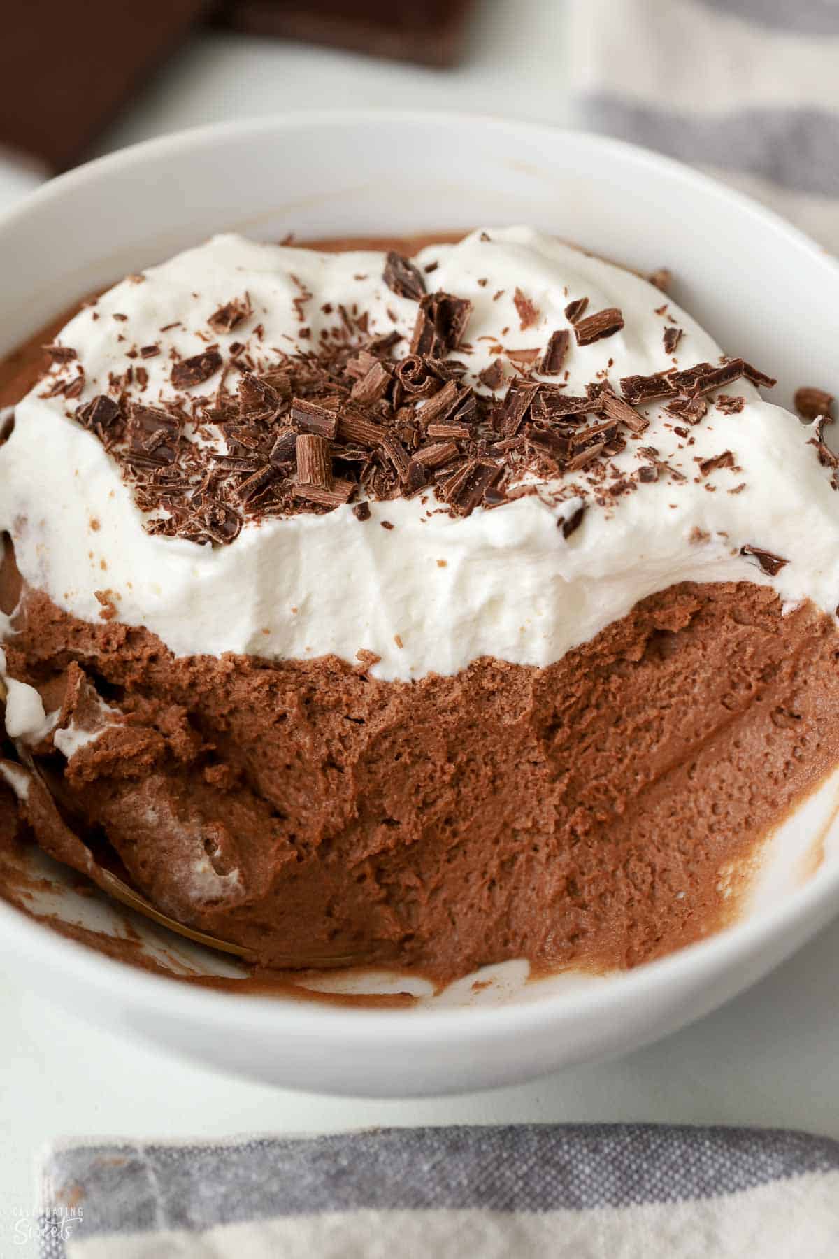 Close up of chocolate mousse topped with whipped cream and chocolate shavings in a white bowl.