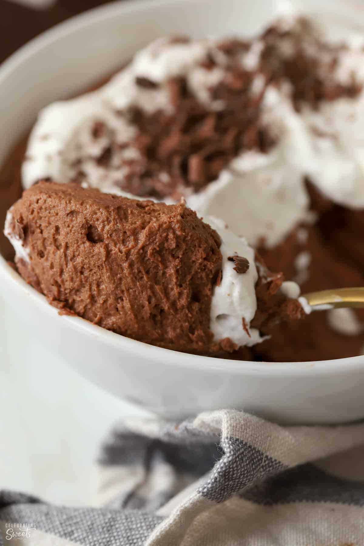 Closeup of a spoonful of chocolate mousse on a gold spoon sitting on a white bowl.