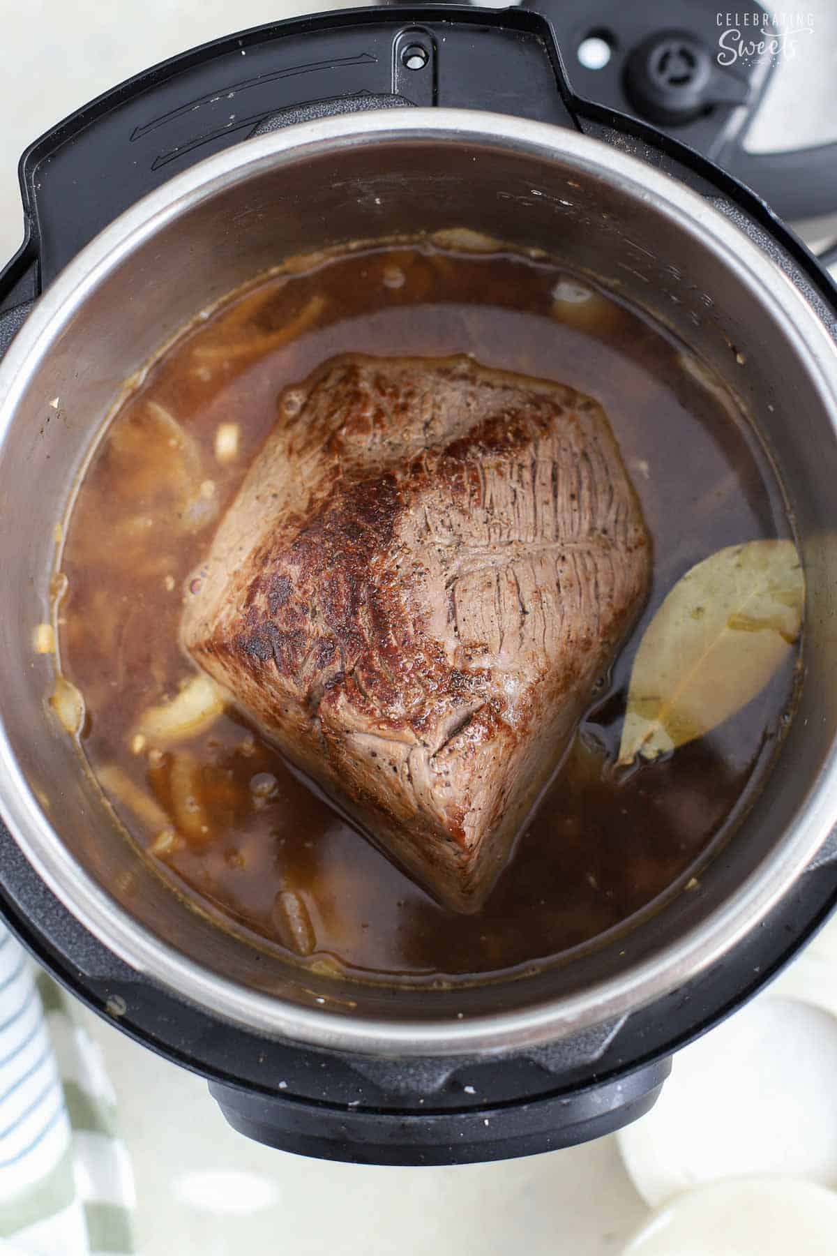 Roast beef in an instant pot with broth and a bay leaf.