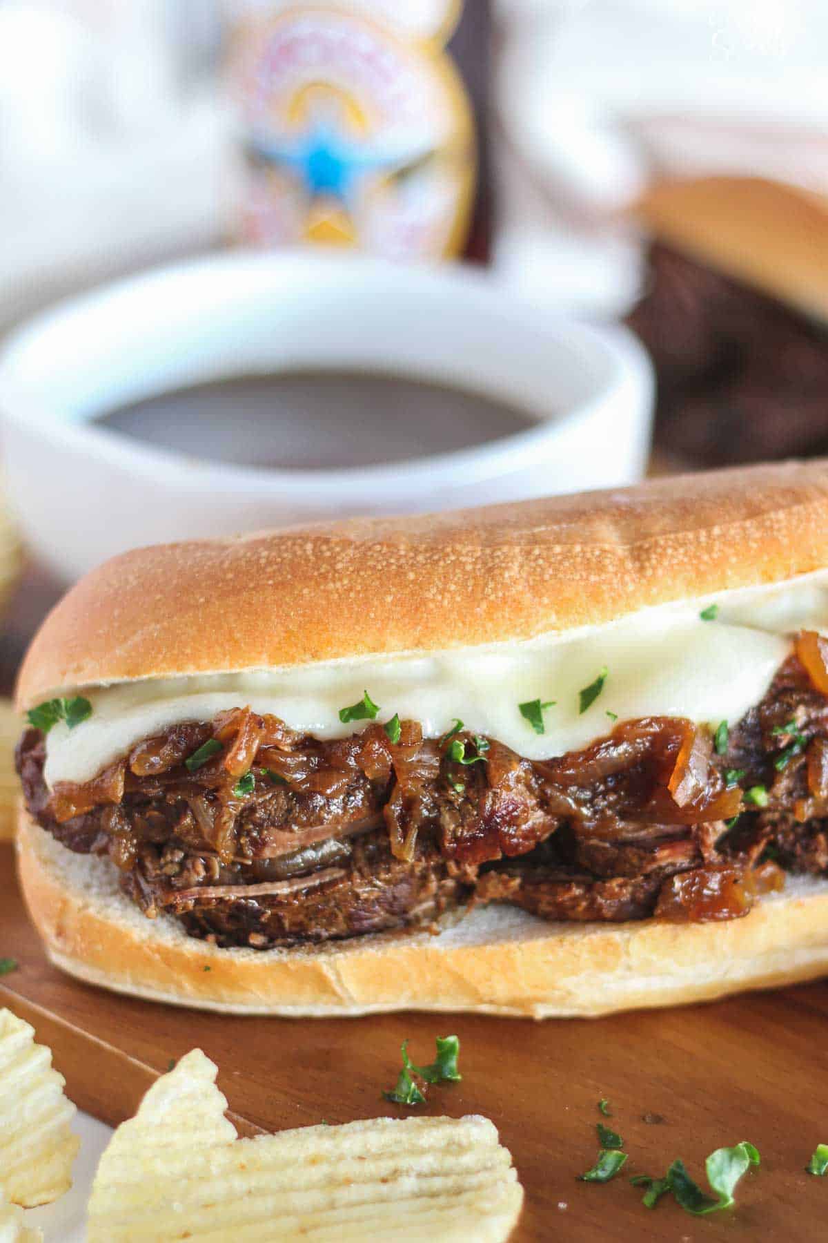 French dip sandwich on a wood cutting board with a white bowl in the background.