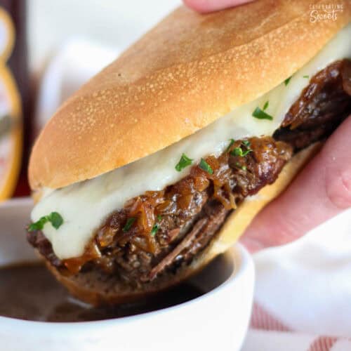 French dip sandwich being dipped in au jus in a white bowl.