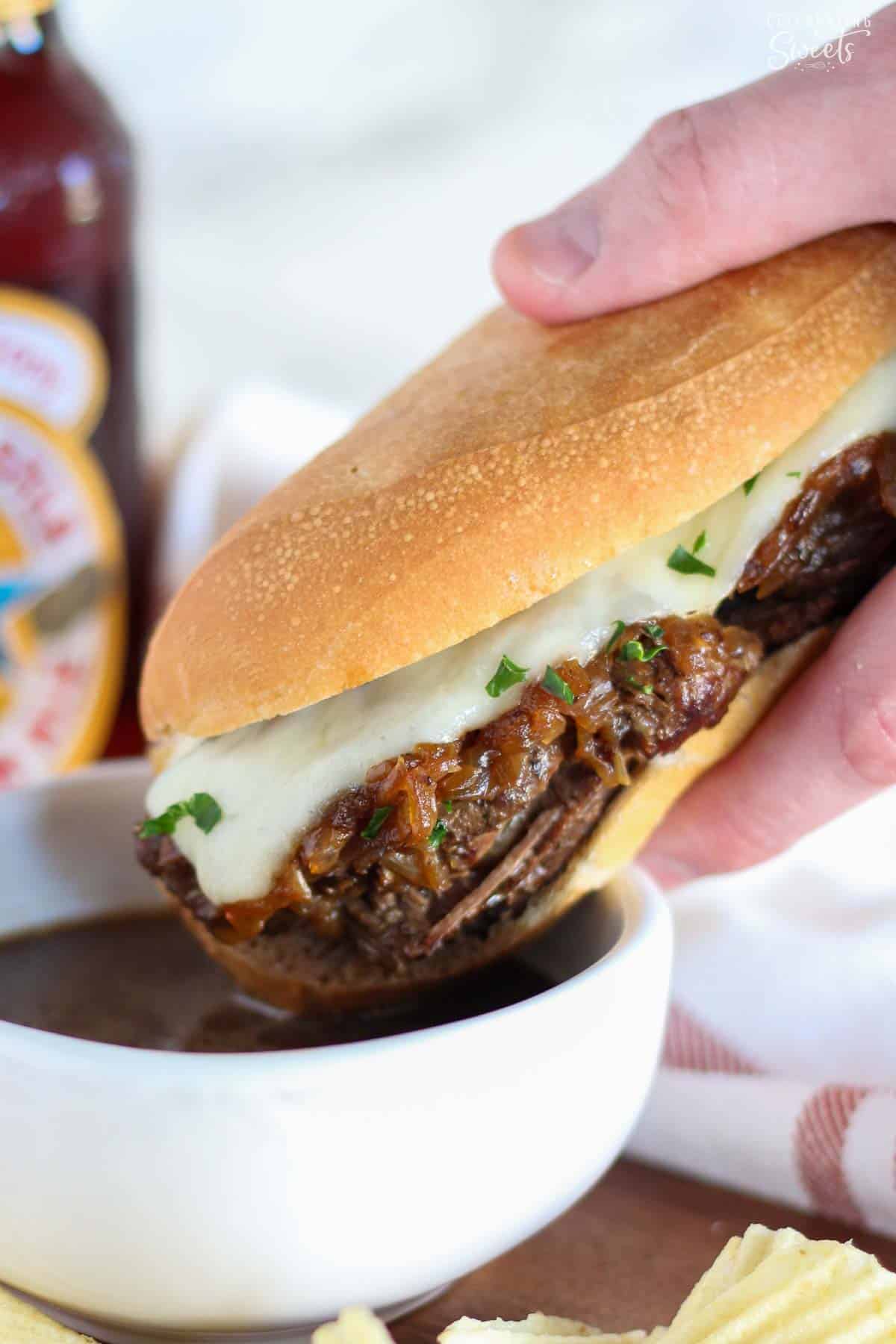 French dip sandwich being dipped in au jus in a white bowl.