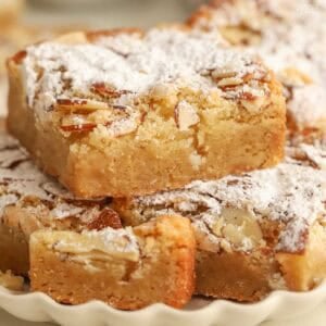 Almond blondies stacked on a beige scalloped plate.