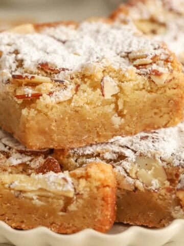 Almond blondies stacked on a beige scalloped plate.