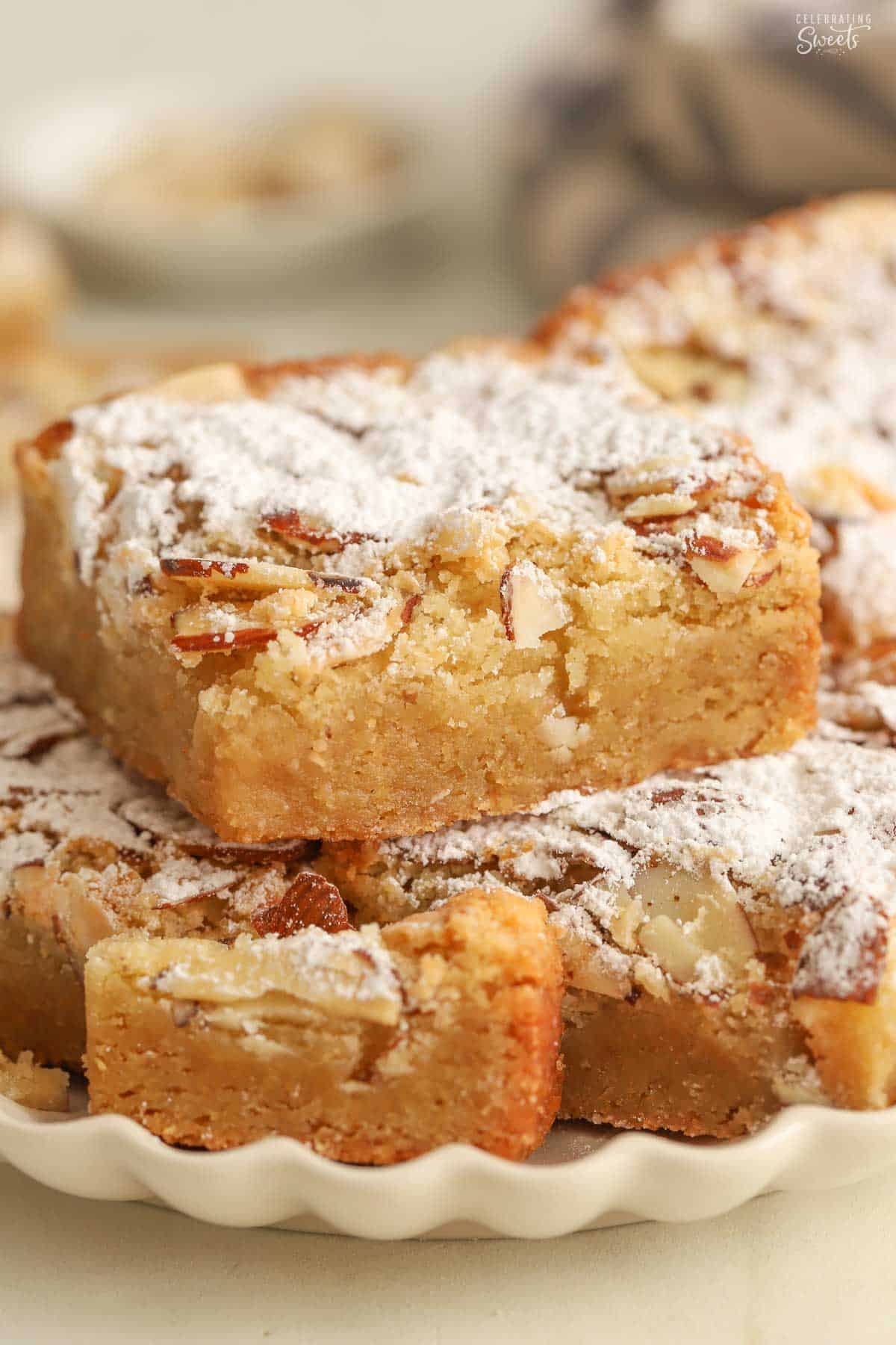 Stack of almond blondies on a beige scalloped plate.